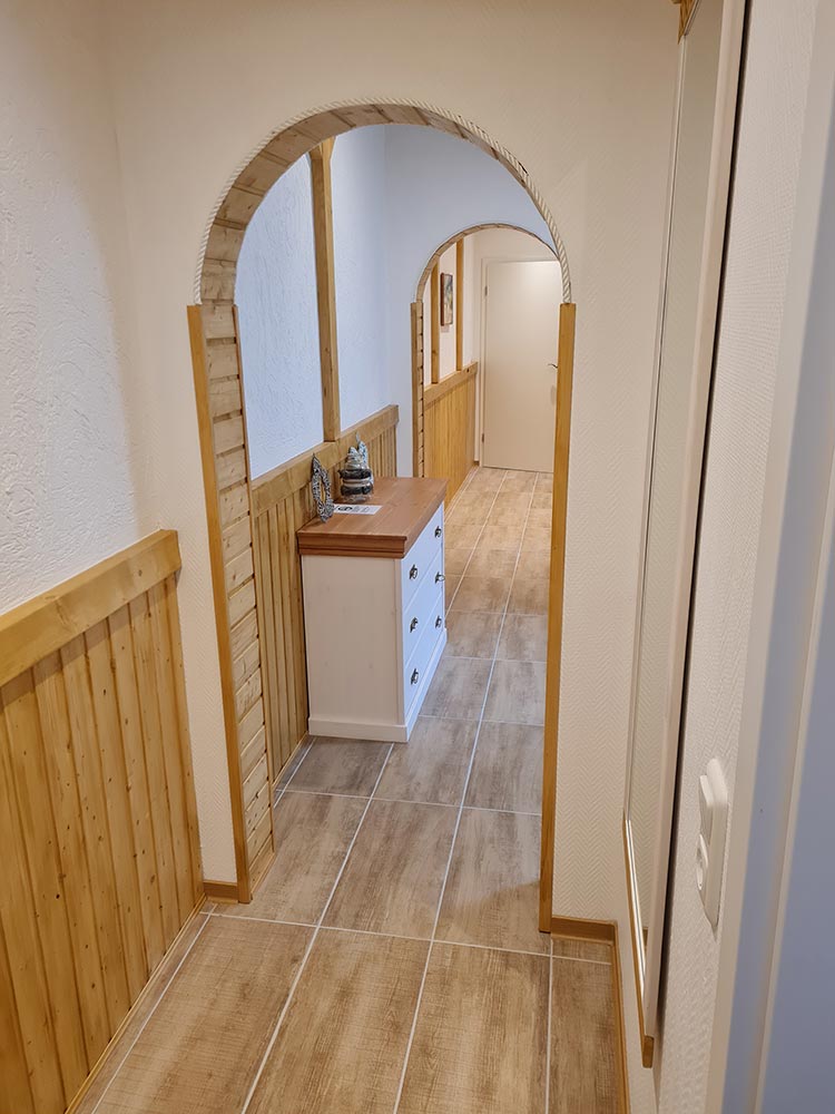 Ein Flur mit Holzwänden, Fliesenboden und einem weißen Schrank mit Dekoration.