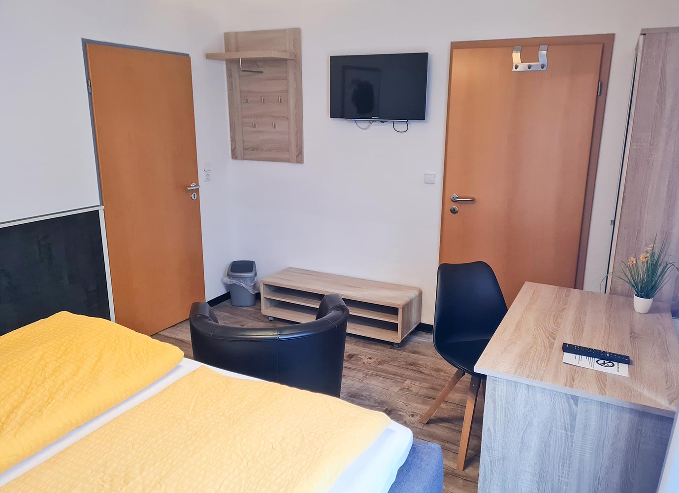 Ein Hotelzimmer mit gelben Bettdecken, Stuhl, Schreibtisch und einem Flachbildfernseher an der Wand.