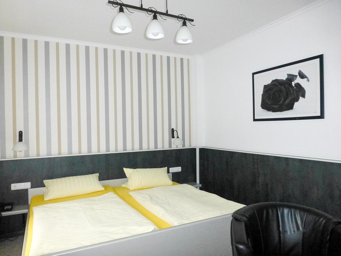 Ein Hotelzimmer mit zwei Einzelbetten, gelber Bettwäsche, gestreifter Wand und schwarzem Kunstwerk.