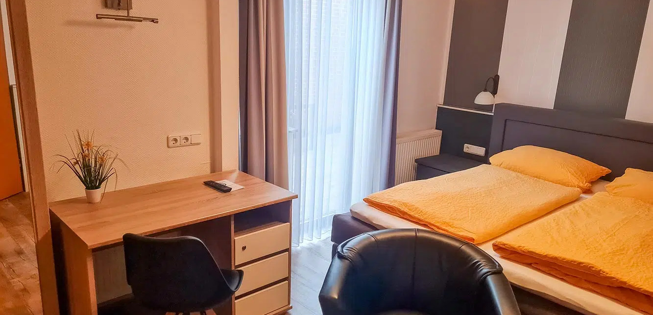 Helles Hotelzimmer mit Schreibtisch, Stuhl und Doppelbett mit gelber Bettwäsche.