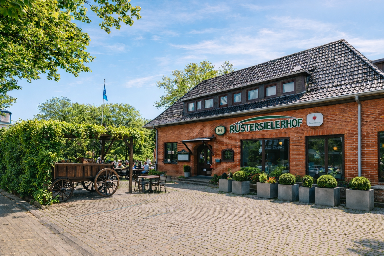 Ziegelrotes Gasthaus mit großen Fenstern und grünem Schild sowie gemütlichem Außenbereich